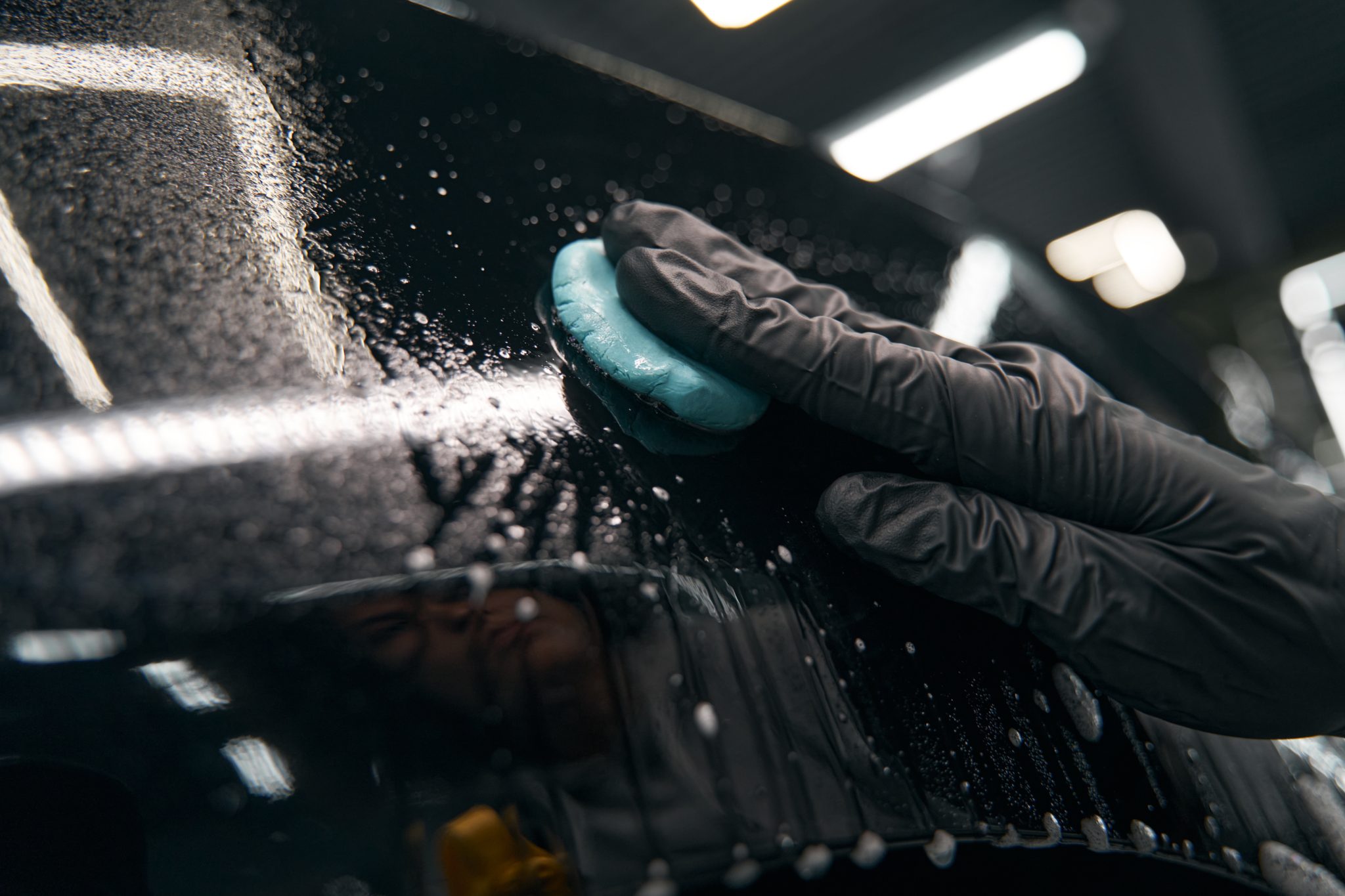 Worker in blue gloves scrubbing dark textured surface with brush under bright lights