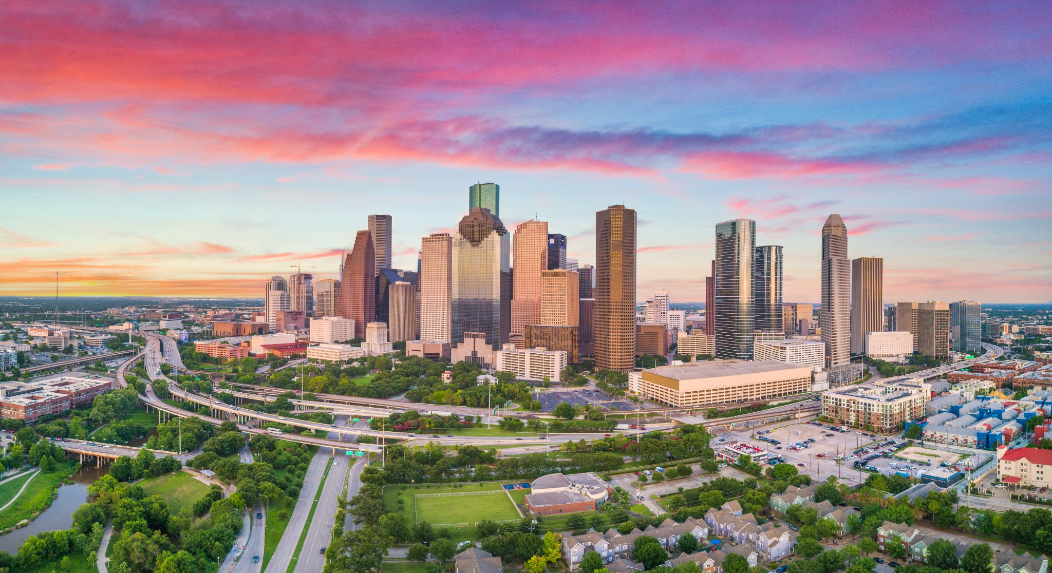 Houston skyline at sunset with downtown towers, highways, and green spaces
