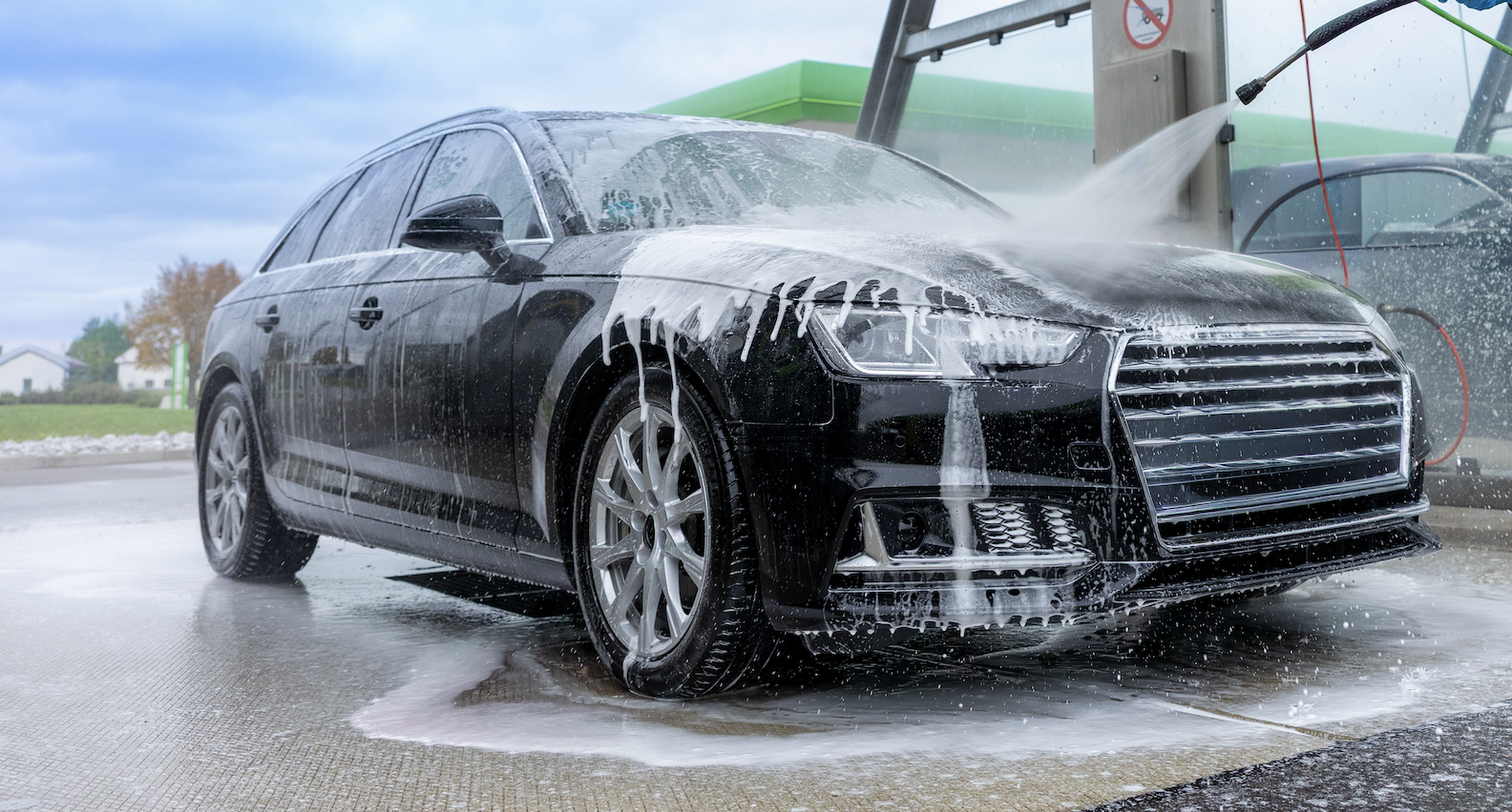 Black SUV being washed at professional car wash station with high-pressure water spray