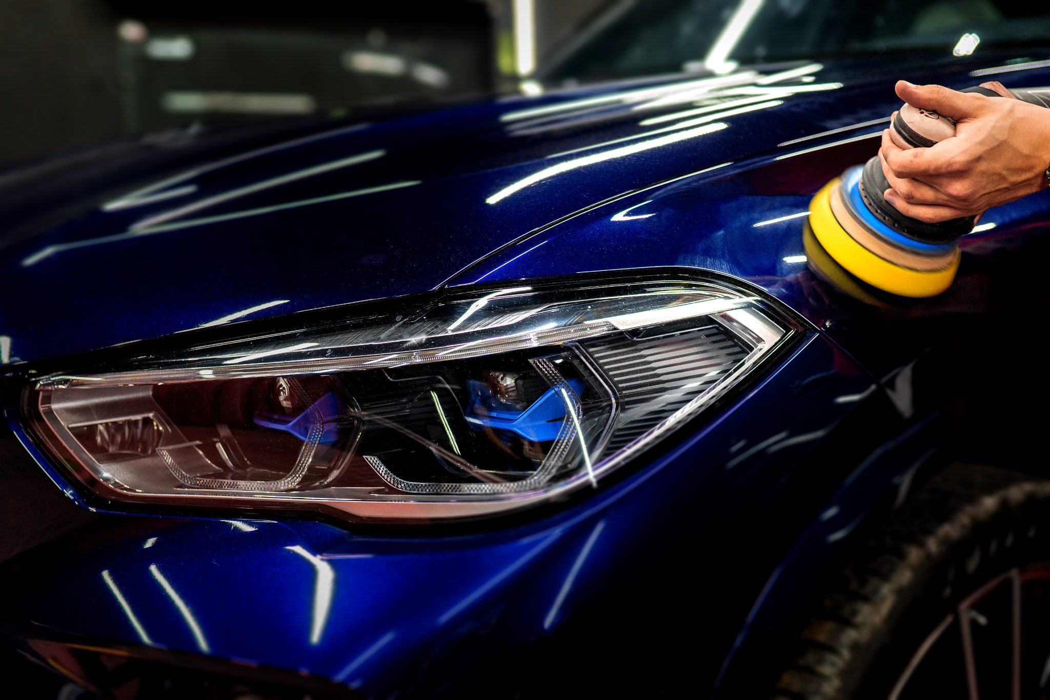 Professional car detailing with polishing pad on blue vehicle headlight