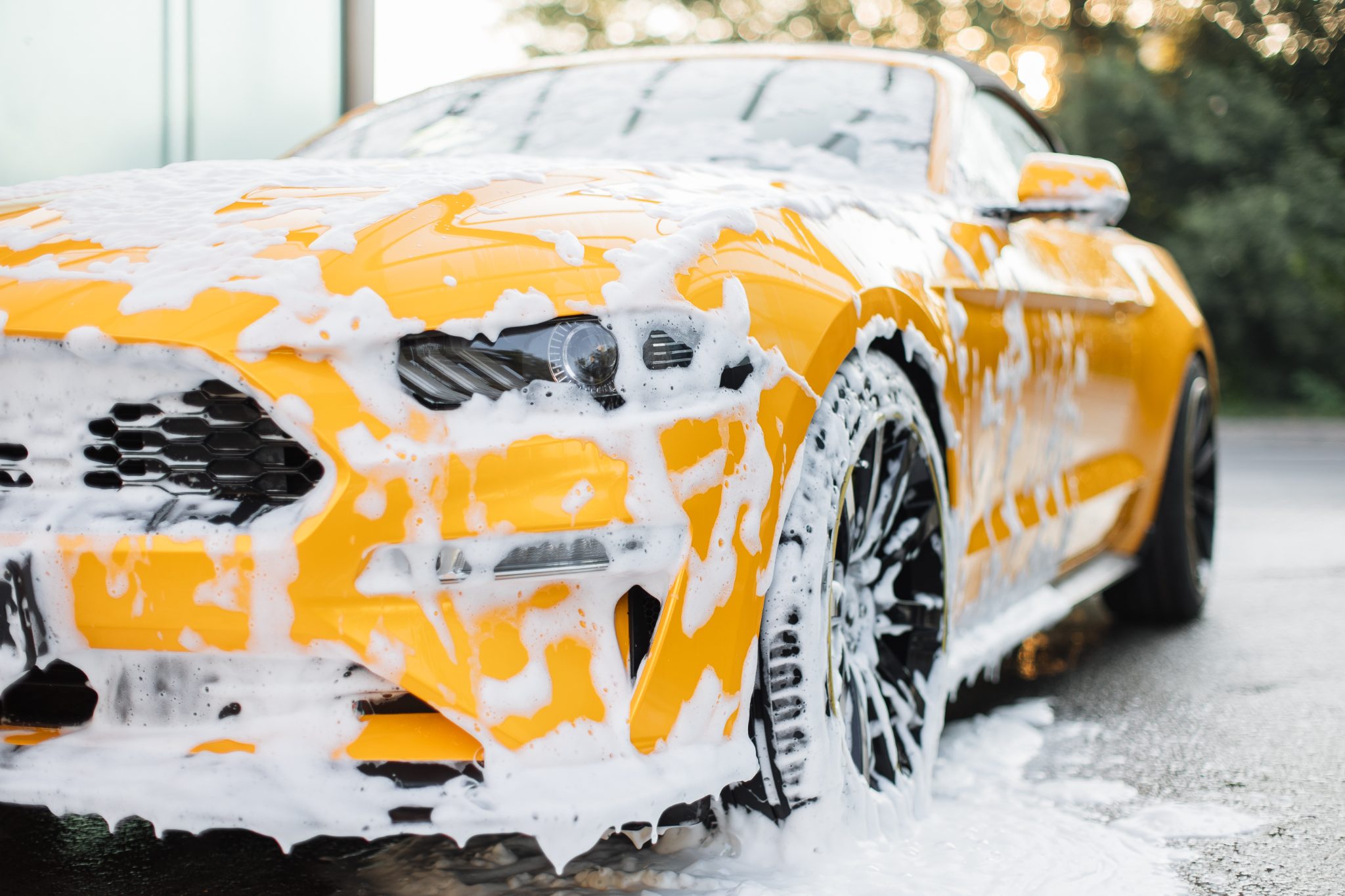 Bright yellow sports car covered in white foam during car wash service