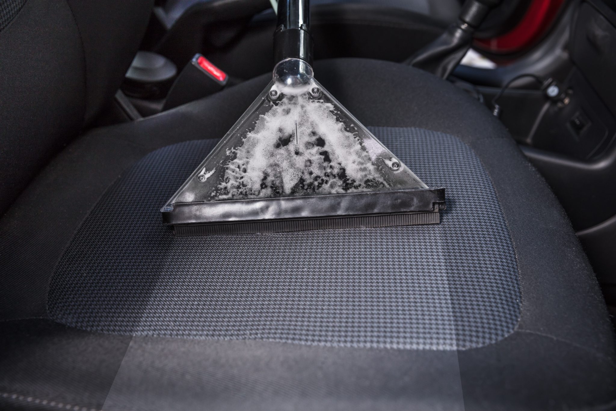 Car interior seat being cleaned with triangular carpet cleaning tool filled with foam