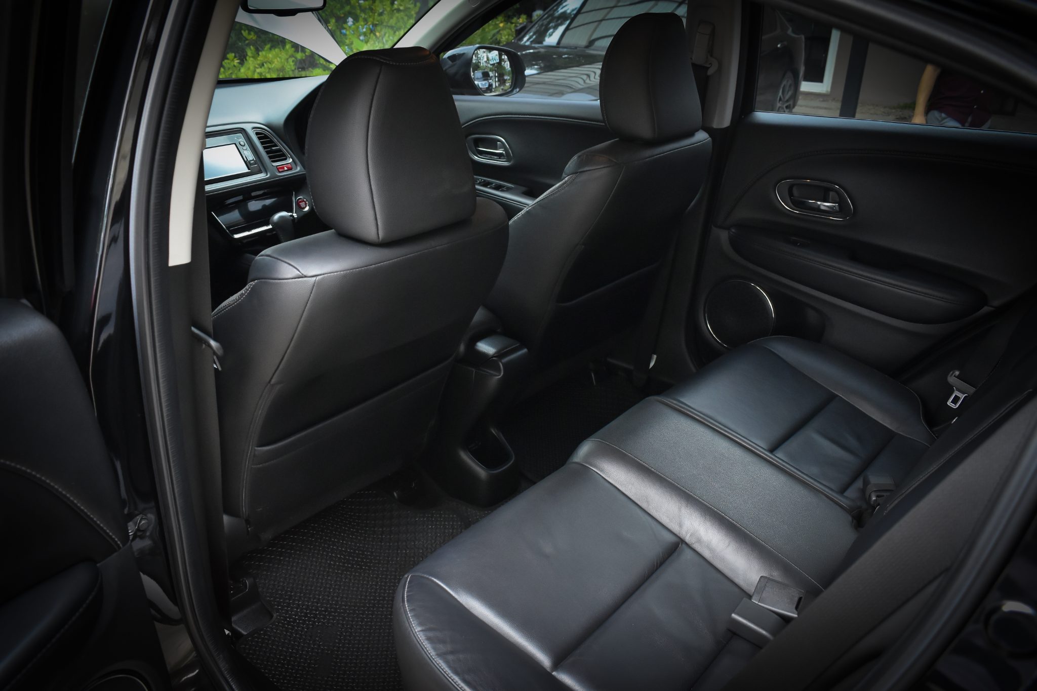 Black leather car interior with front and rear seats, steering wheel, and dashboard visible through open door